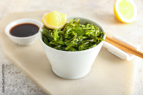 Bowl with healthy seaweed salad, lemon and sauce on light background