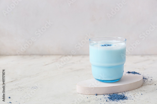 Glass of blue matcha tea and powder on light background