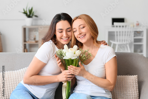 Young woman and her mother with flowers on International Women's Day at home