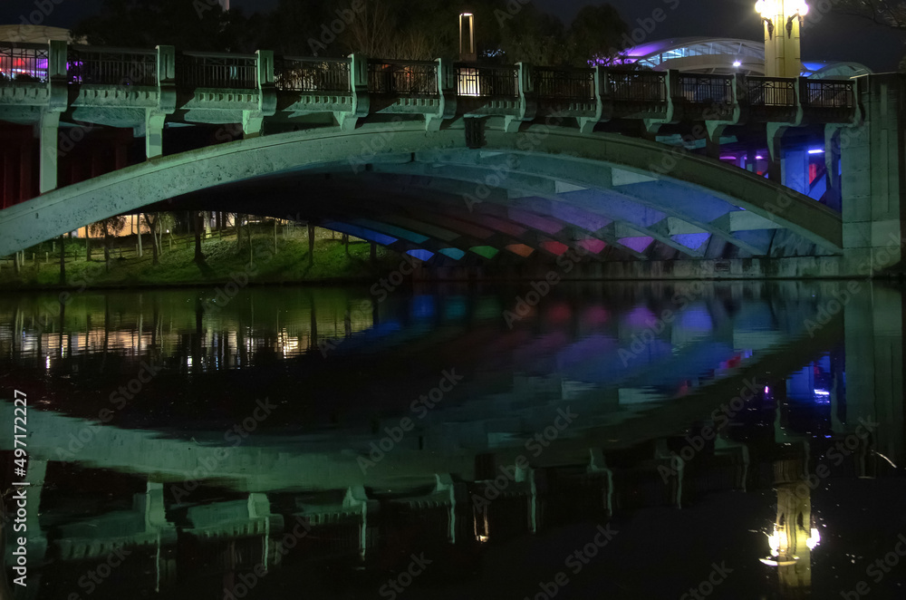 Night cityscape with a bridge with colourful lanterns and reflection in the water