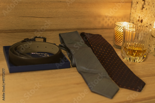 Vintage table with two ties, belt, candlelight and whisky.