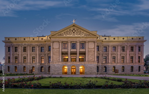 Illuminated Arizona State Capitol in Phoenix at dusk.  Beautiful glowing orange lights coming from the windows lighting up the rose garden.
