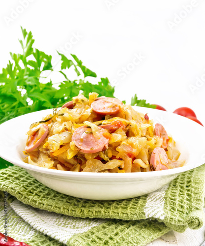 Cabbage stew with sausages in white plate on wooden board