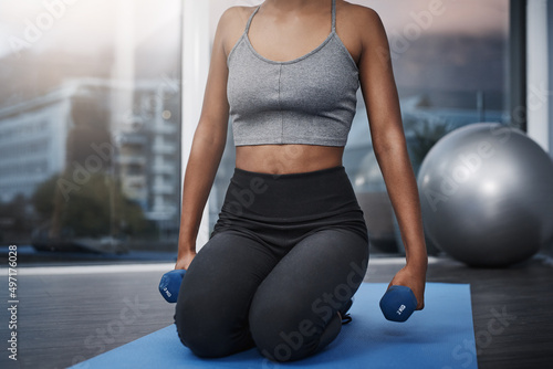 Consistency is always key. Cropped shot of an unrecognizable young woman on her knees holding dumbbells while exercising on her gym mat at home.