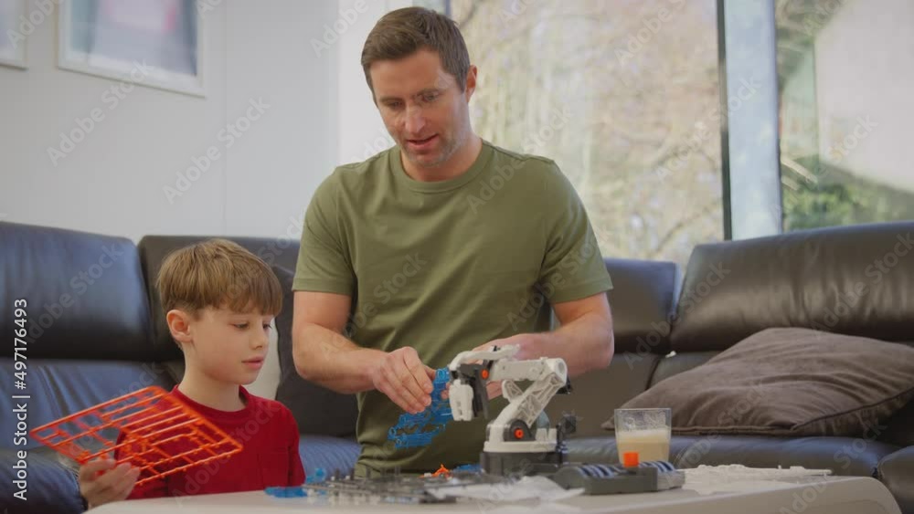 Father and son wearing pyjamas building robotic arm from plastic kit at home for science project - shot in slow motion Father and son wearing pyjamas building robotic arm from plastic kit at home for science project - shot in slow motion