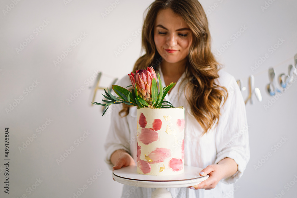 Young woman with birthday cake, close up. The cake is decorated with protea flowers. Holiday and confectionery concept Young woman with birthday cake, close up. The cake is decorated with protea flowers. Holiday and confectionery concept
