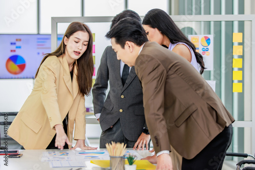 Millennial Asian young professional successful male and female businessman businesswoman worker employee in formal suit standing discussing brainstorming together at working desk in company office photo