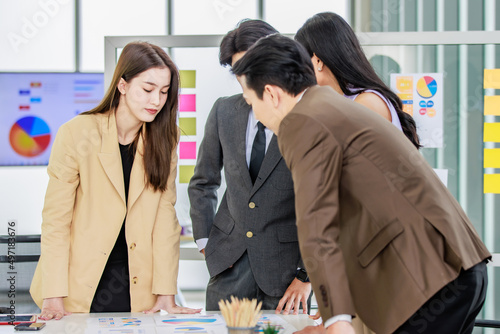 Millennial Asian young professional successful male and female businessman businesswoman worker employee in formal suit standing discussing brainstorming together at working desk in company office photo