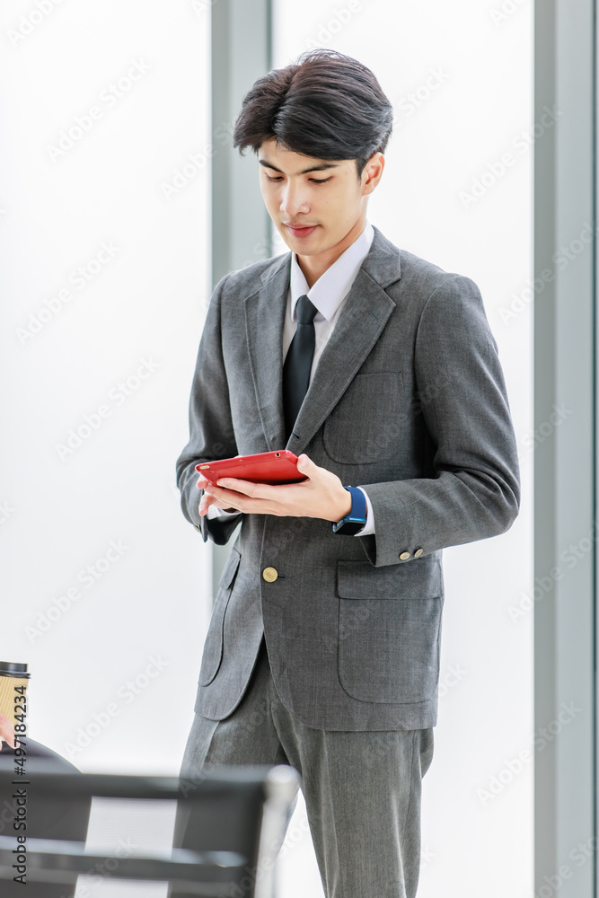 Asian male professional businessmen colleague in formal business suit take coffee break standing holding disposable paper cup and tablet computer talking have conversation together in front monitor Asian male professional businessmen colleague in formal business suit take coffee break standing holding disposable paper cup and tablet computer talking have conversation together in front monitor
