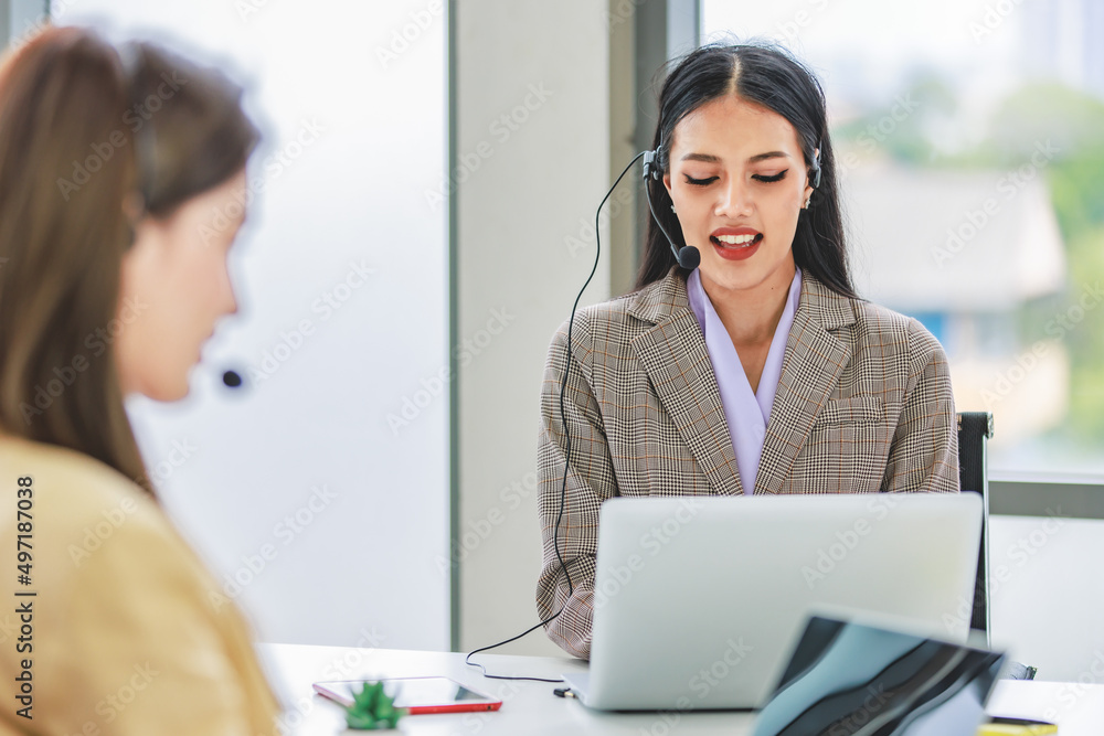 Asian young beautiful happy female businesswoman customer service call center operater in formal business suit sitting at working desk chat online with client via microphone headset in company office Asian young beautiful happy female businesswoman customer service call center operater in formal business suit sitting at working desk chat online with client via microphone headset in company office