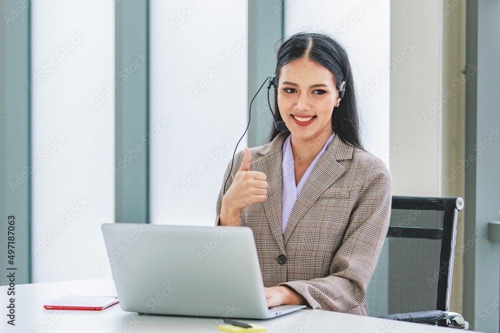 Asian young beautiful happy female businesswoman customer service call center operater in formal business suit sitting at working desk chat online with client via microphone headset in company office Asian young beautiful happy female businesswoman customer service call center operater in formal business suit sitting at working desk chat online with client via microphone headset in company office