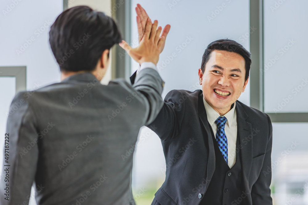 Closeup shot of Asian happy professional successful male businessman employee in formal business suit standing smiling holding high five with unrecognizable unknown colleague in blurred foreground Closeup shot of Asian happy professional successful male businessman employee in formal business suit standing smiling holding high five with unrecognizable unknown colleague in blurred foreground
