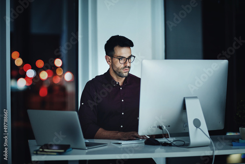 Staying late to get it done. Shot of a young businessman using a computer at his desk during a late night at work.