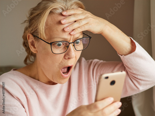 Fotografie Senior woman dumbfounded by the news looks into the smartphone