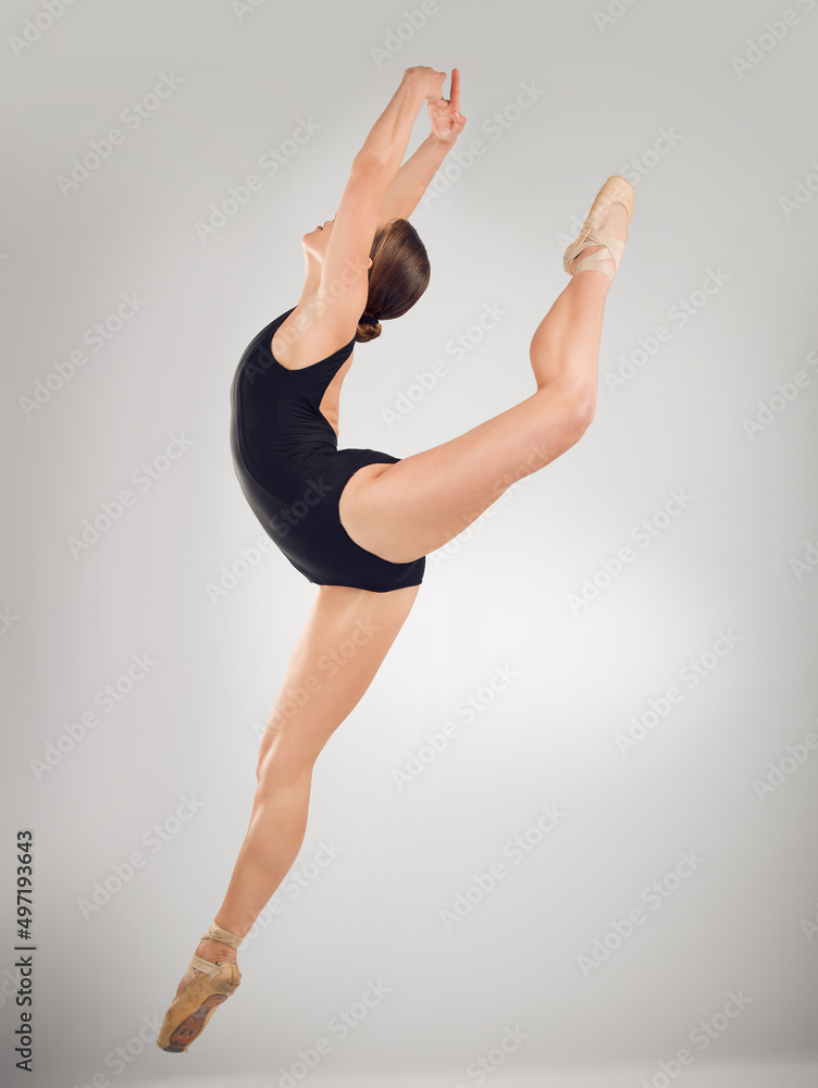 Perfect form is required. Full length shot of an attractive young female ballet dancer in studio against a grey background.