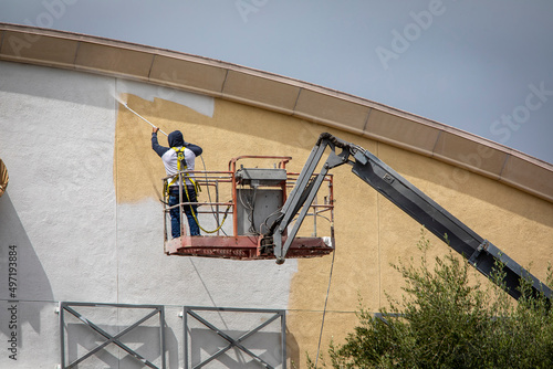 Man painting a yellow wall white using a paint sprayer while standiong on a manlift photo