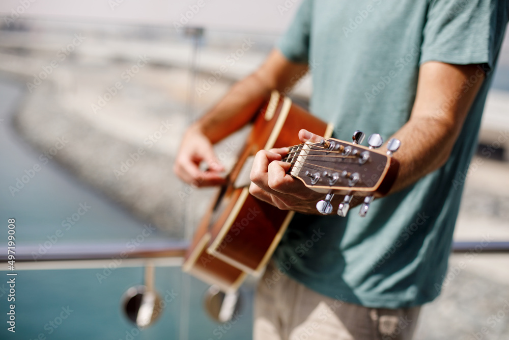 Close-up of a man playing a classical guitar while sitting on the beach in summer. Lifestyle, rest, relaxation Close-up of a man playing a classical guitar while sitting on the beach in summer. Lifestyle, rest, relaxation