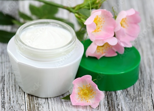 Cosmetic cream with pink flower wild rose. Moisturizer cream with flowers on the white wooden table.