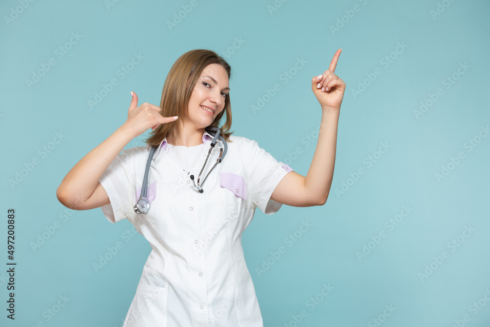 A woman doctor shows a symbol of a phone and with her hand points to a method for advertising or a phone number, on a blue background. Copy paste. healthcare concept. A woman doctor shows a symbol of a phone and with her hand points to a method for advertising or a phone number, on a blue background. Copy paste. healthcare concept.