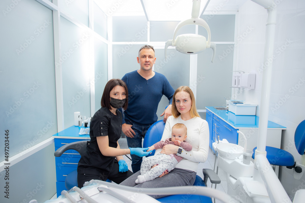 Young parents and their daughter visit a dentist to examine milk teeth. Baby at the first appointment with the dentist. Inspection of the formation of jaws, eruption of milk teeth. Young parents and their daughter visit a dentist to examine milk teeth. Baby at the first appointment with the dentist. Inspection of the formation of jaws, eruption of milk teeth.