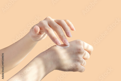 Concept of self-care. Application of cream, lotion on hands. Beautiful female hands rub moisturizing liquid into delicate skin in the rays of sunlight. Close-up, beige isolated background photo