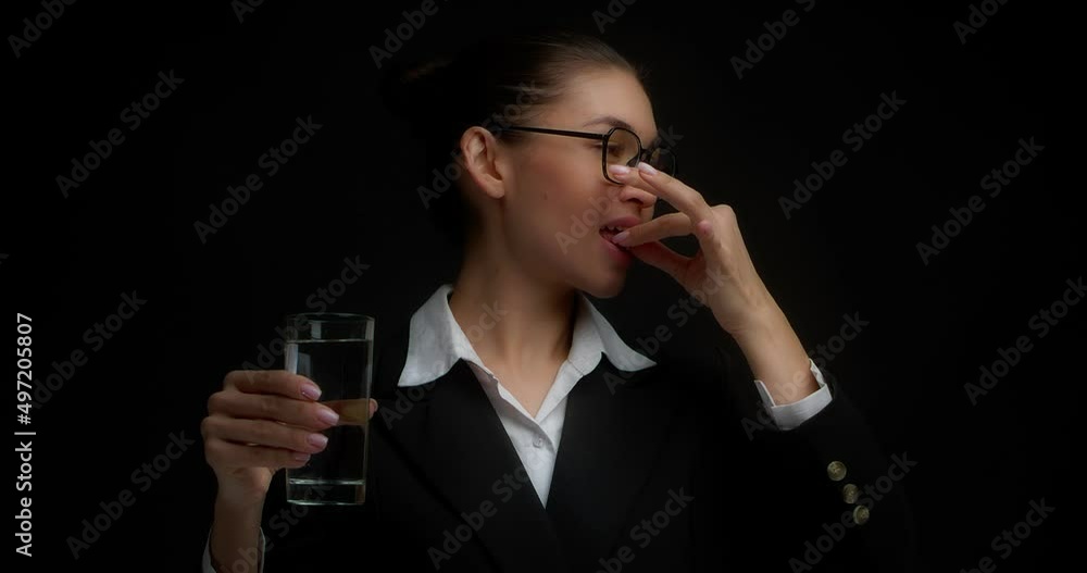 Cheerful business woman in glasses with her hair gathered, holds a tablet, a vitamin in her hands and washes it down with water from a glass, gives a thumbs up. Isolated on a black background Cheerful business woman in glasses with her hair gathered, holds a tablet, a vitamin in her hands and washes it down with water from a glass, gives a thumbs up. Isolated on a black background