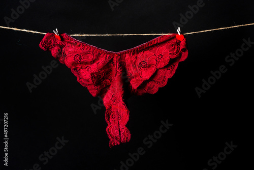 Womans erotic red underwear panties hanging on rope isolated on black background. Lace lingerie, woman sexy underwear.