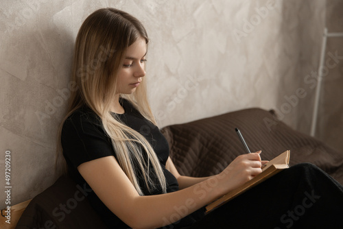 beautiful girl works at home lying on the bed and makes notes in a notebook