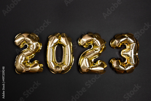 Golden foil balloons in the shape of figure 2023 on a black background. The concept of celebrating the new year.