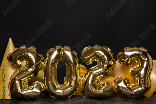 Golden foil balloons in the shape of figure 2023 on a black background. The concept of celebrating the new year.