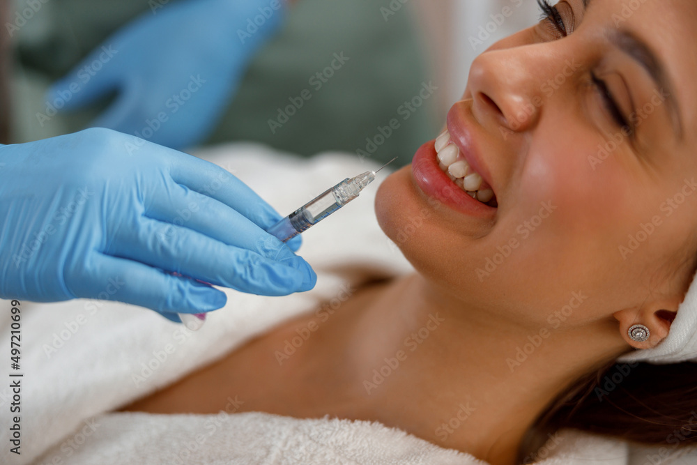 Smiling young woman getting hyaluronic acid injections in lips at beauty salon. Cosmetology Smiling young woman getting hyaluronic acid injections in lips at beauty salon. Cosmetology