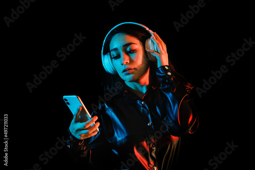 latin young woman with headphones listening to music over color neon and black background in Mexico Latin America