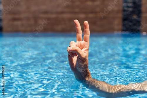 Man chilling in the water in pool and showing signs ok with his hand