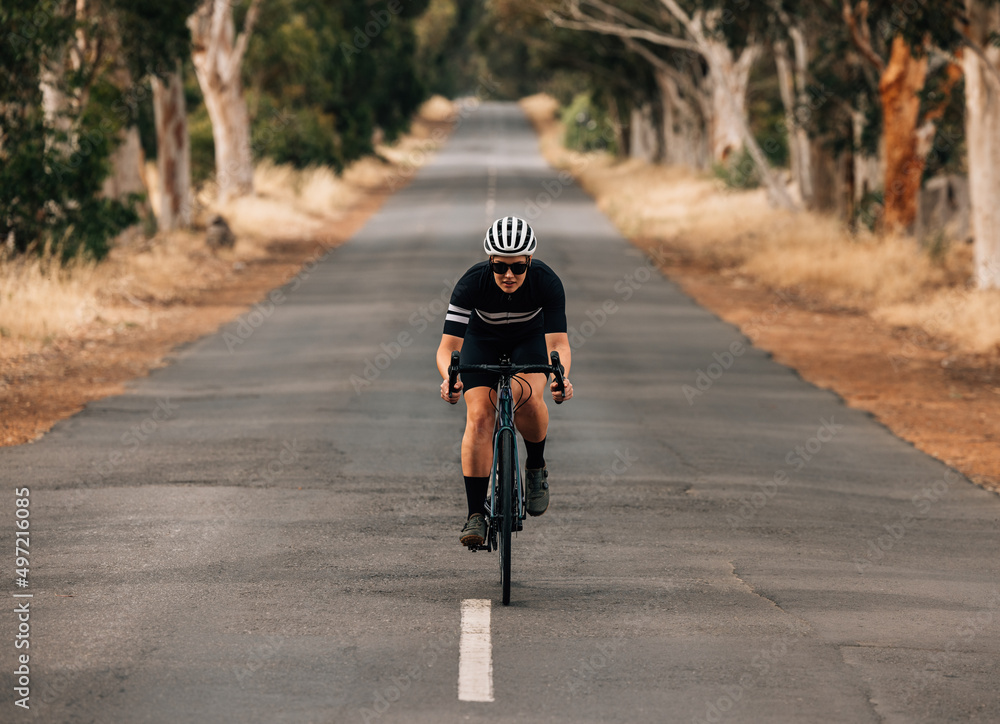 Athlete cycling on empty country road. Professional cyclist training outdoors.