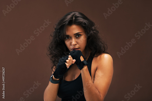 Woman in sport gloves posing in combat stance looking at camera against brown background