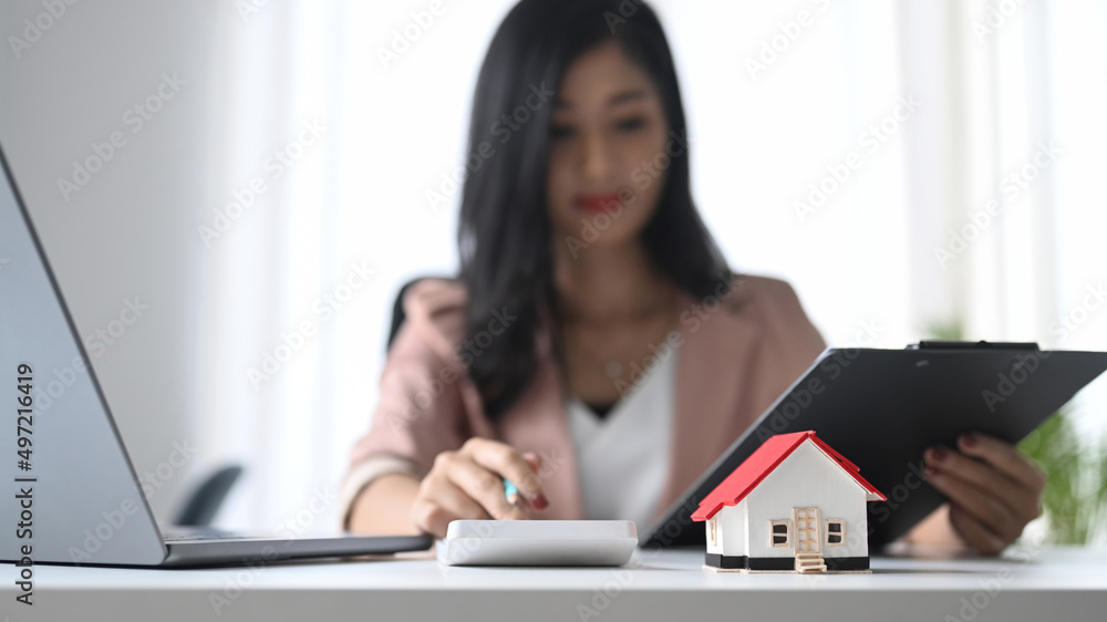 Small house model on white table and professional financial advisor is using calculator. Small house model on white table and professional financial advisor is using calculator.