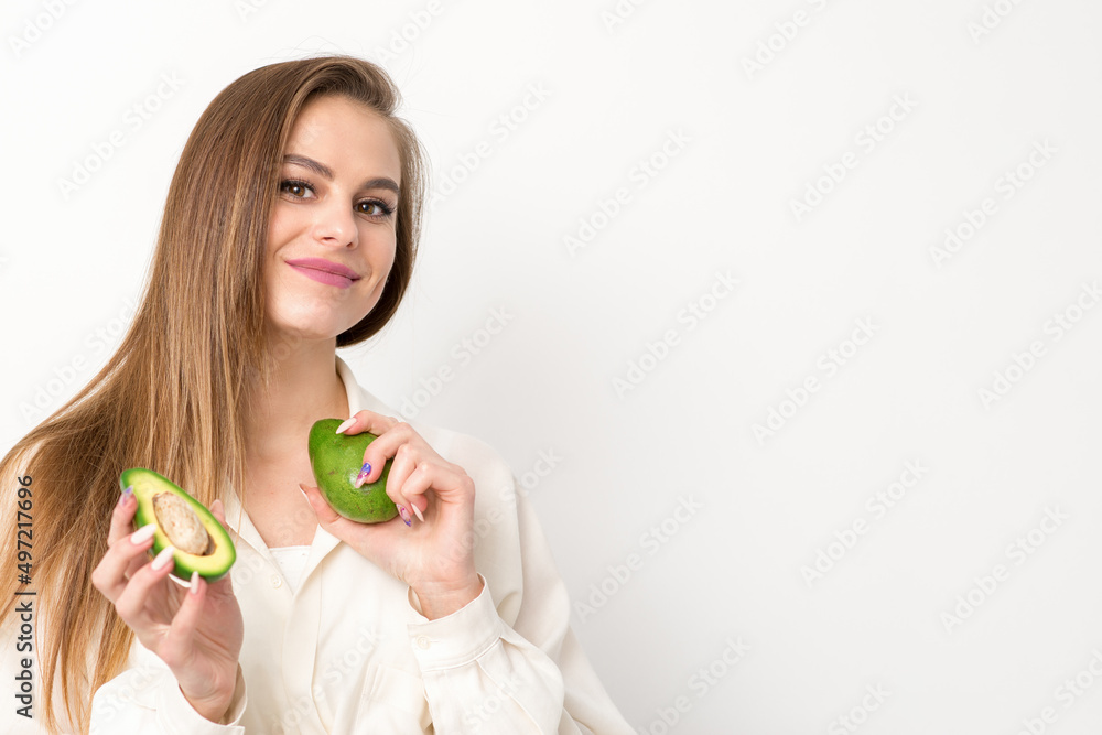 Portrait of a lovely smiling young brunette caucasian woman wearing the white shirt with long hair holding and showing avocado, standing isolated over white background Portrait of a lovely smiling young brunette caucasian woman wearing the white shirt with long hair holding and showing avocado, standing isolated over white background