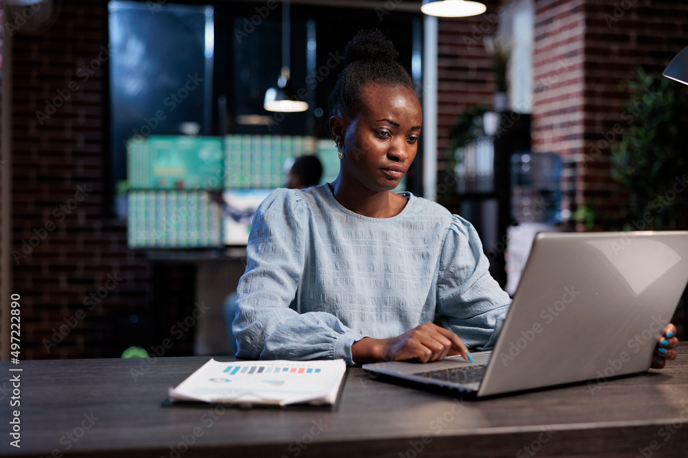 Forex stock market professional trader sitting at desk with laptop while buying and selling trading options. African american woman sitting in office workspace while analyzing real time financial data Forex stock market professional trader sitting at desk with laptop while buying and selling trading options. African american woman sitting in office workspace while analyzing real time financial data
