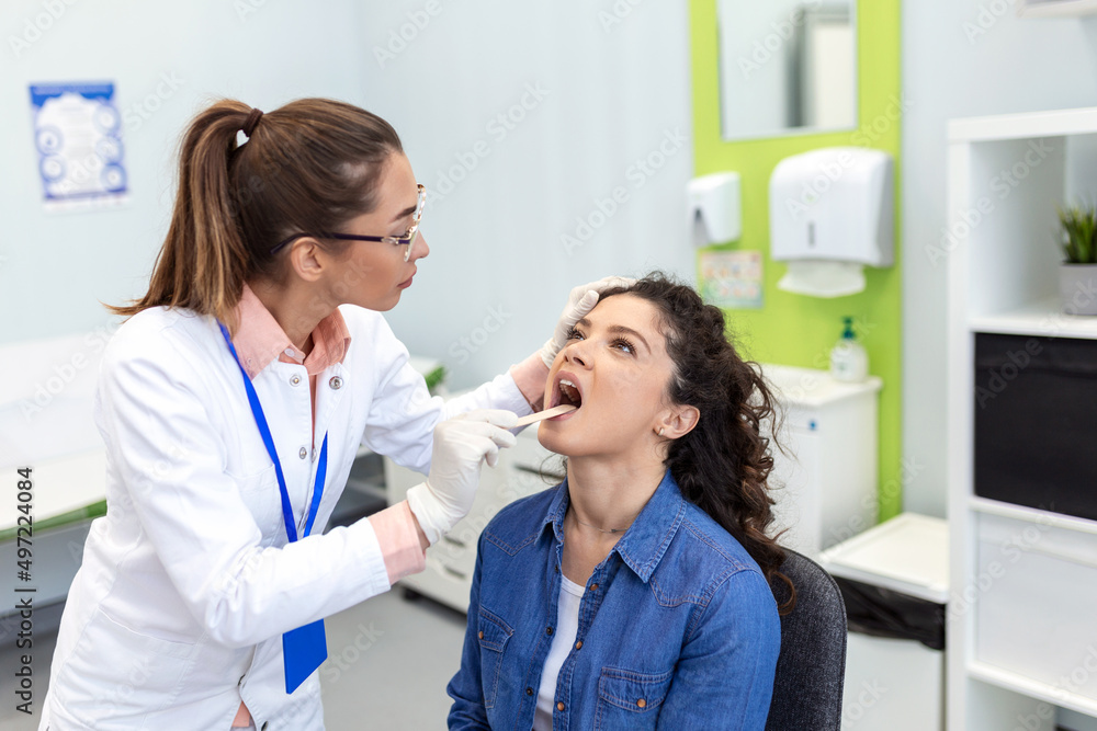 Fototapeta premium Doctor with depressor checking sore throat. Experienced doctor examines adult woman for sore throat