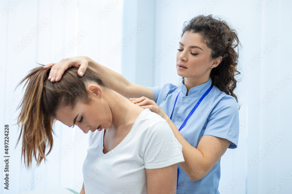 Fototapeta premium Licensed chiropractor or manual therapist doing neck stretch massage to relaxed female patient in clinic office. Young woman with whiplash or rheumatological problem getting professional doctor's help