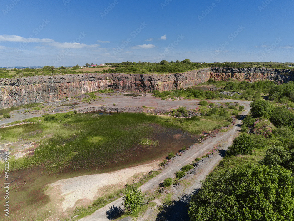 Abandoned stone quarry filled with water. Construction material production. Heavy industry impact on ecology. Aerial drone view. Warm sunny day.