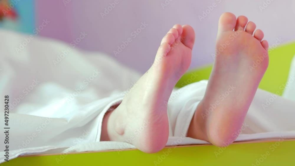 Bare feet of a child on a white bed and a green bed. Paws move from side to side. Lazy morning, awakening. Bare feet of a child on a white bed and a green bed. Paws move from side to side. Lazy morning, awakening.
