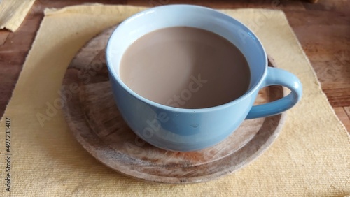 Große Kaffeetasse mit Milchgetränk. Nahaufnahme. Eine Holzplatte unter der Tasse. Gelbe Tischdecke. Ländliche Szene. Holzsockel. Geschirr aus Porzellan. Heißes Getränk. Erfrischung in der Pause. Heiß.