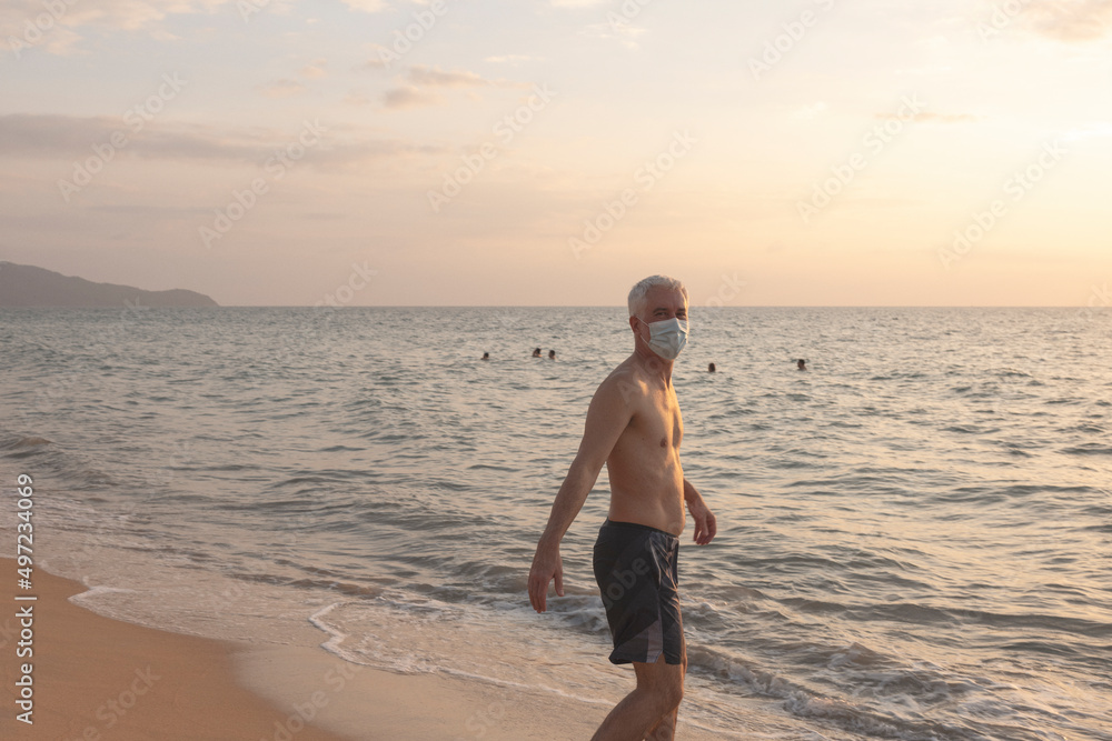 Senior man walking on beach in protective face mask Senior man walking on beach in protective face mask