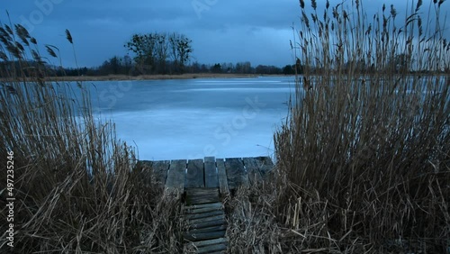 Reeds and a wooden pier by the shore of a frozen lake, a windy day, Stankow, Poland photo