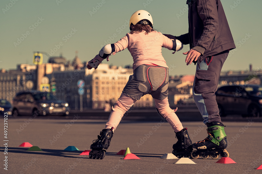 A child learns to roller skate with a trainer outdoors. The girl performs tricks on roller skates. School for rollerbladers.
