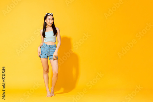 Young pretty Asian woman wearing summer outfit looking sideways to empty space in studio isolated yellow color background photo