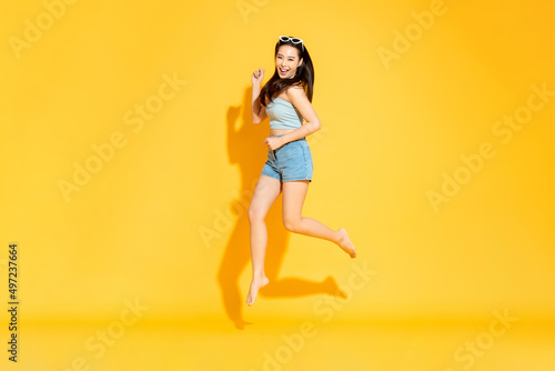 Pretty Asian woman in summer outfit smilng and jumping in studio isolated yellow color background