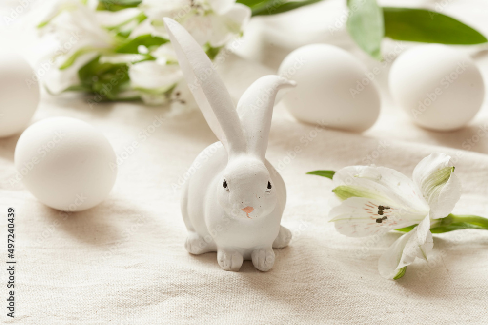 White easter rabbit, white flowers and white eggs on light rustic background, close-up White easter rabbit, white flowers and white eggs on light rustic background, close-up