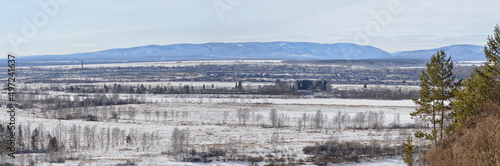 Panorama of the area of the river valley, along which a small town is located. The blue mountains of Sayana are visible on the horizon. Spring landscape in March. Nature of Eastern Siberia © Nadezhda
